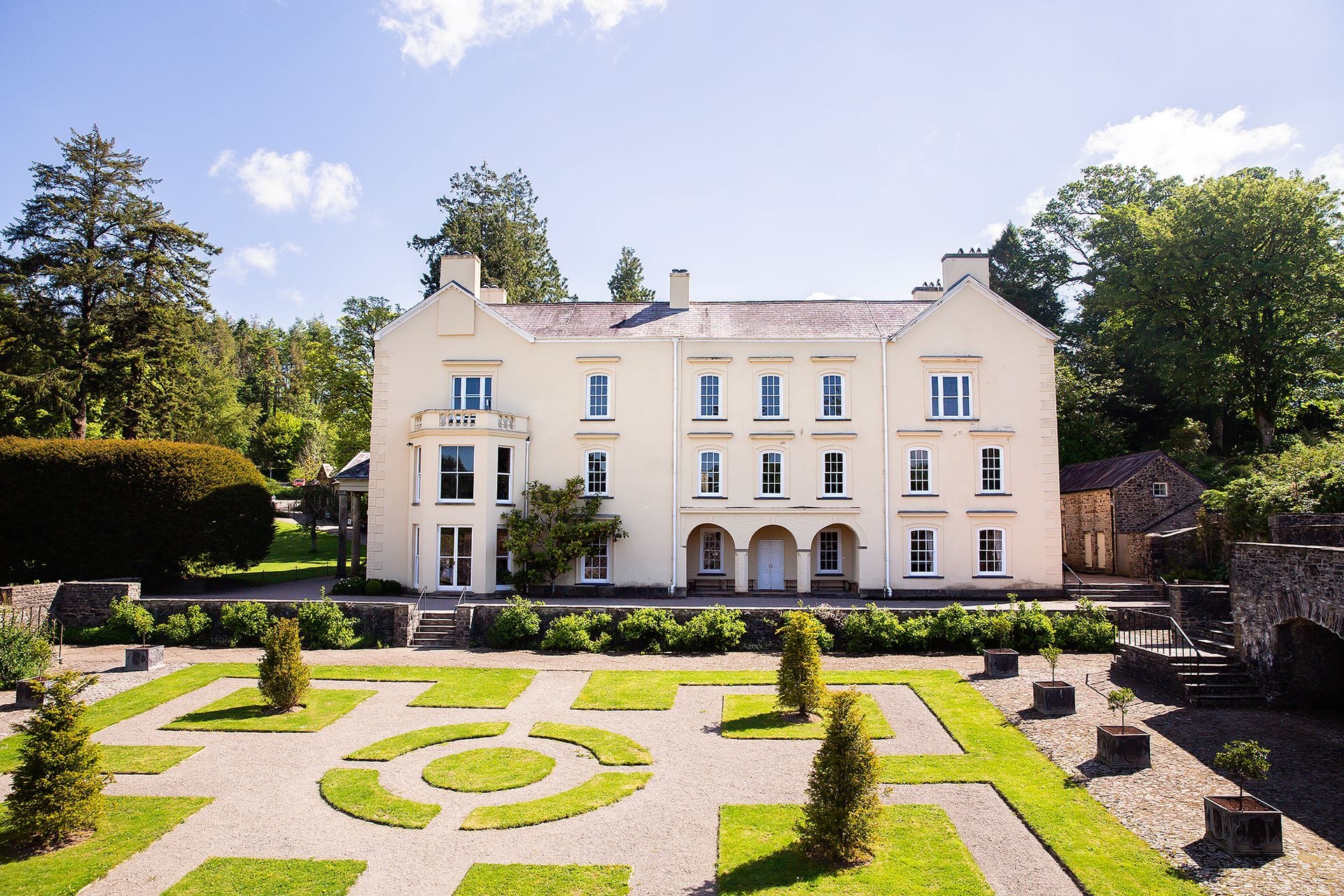 A grand cream-coloured historic mansion surrounded by formal geometric gardens, typical of the premium large group cottages wales offers for luxury holidays and events.