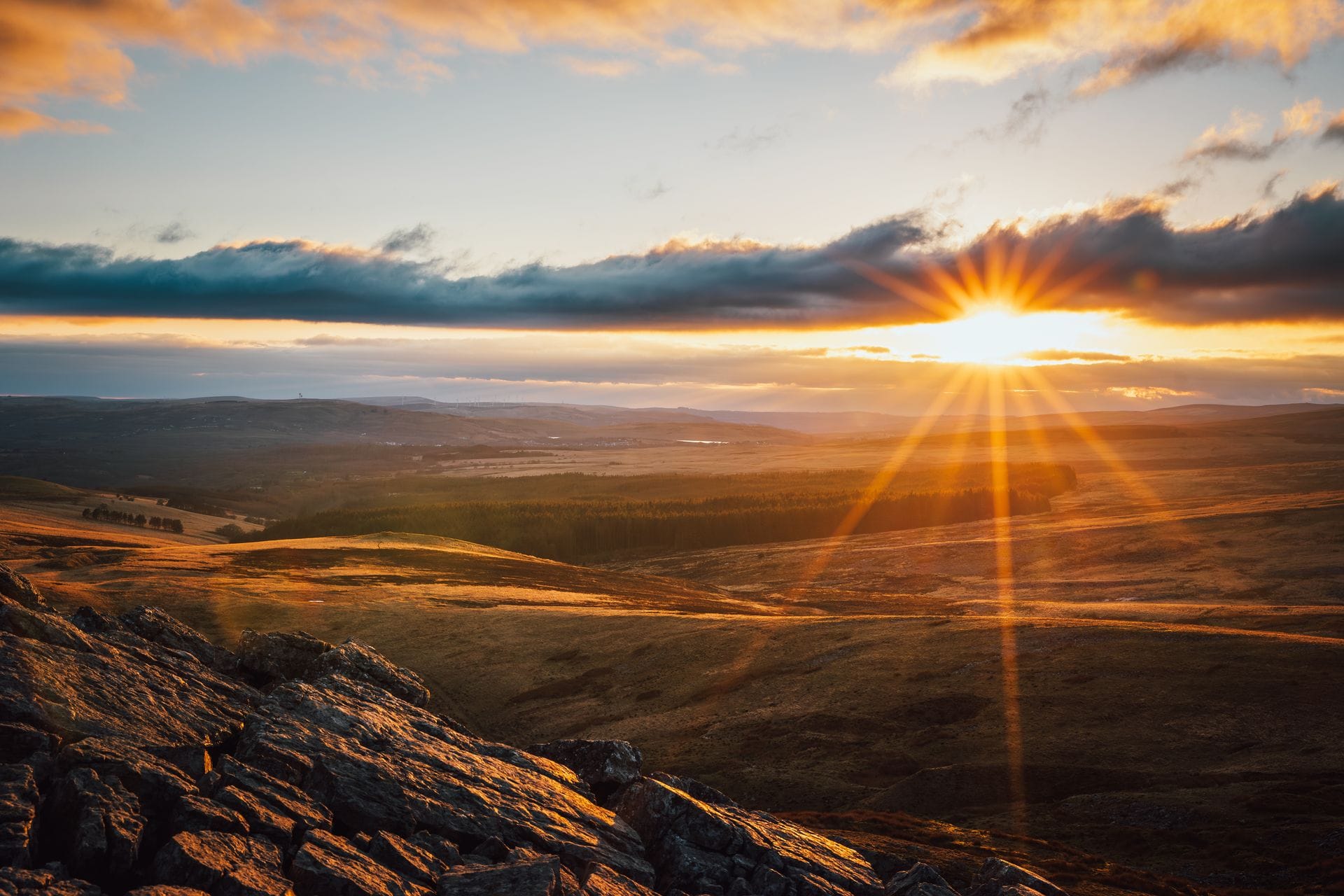 A sunburst golden sunset over the rolling mountain ridges and rocky crags of Bannau Brycheiniog (Brecon Beacons), providing an accessible escape for visitors along the M4 corridor