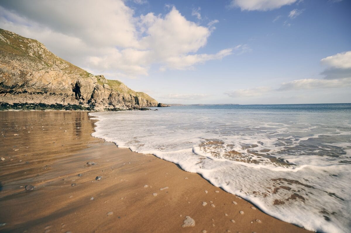 Gentle waves washing onto the sandy shore of Barafundle Bay, backed by rugged green cliffs, highlighting why it's considered one of the best beaches in Pembrokeshire.