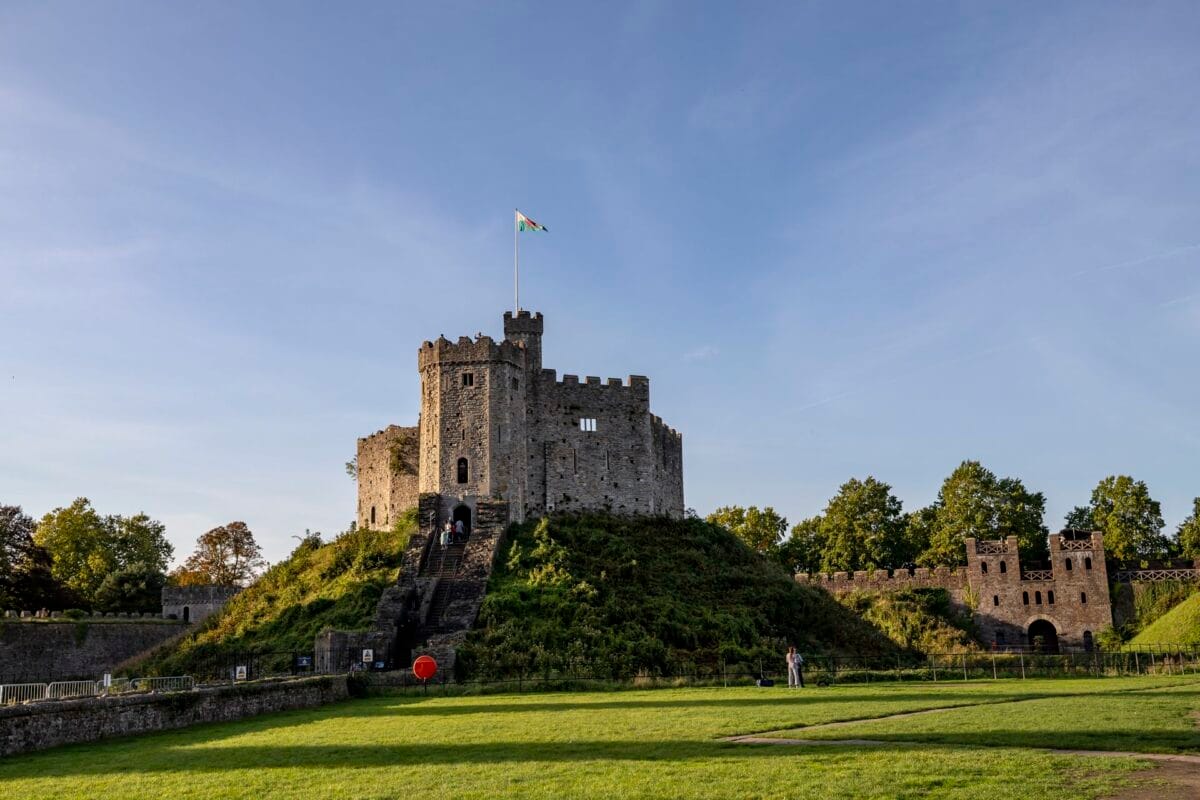 A bright, sunny view of the medieval Norman Keep at Cardiff Castle. The stone fortress sits atop a steep green hill with stairs leading to the entrance, showcasing one of the most popular things to do in Cardiff.