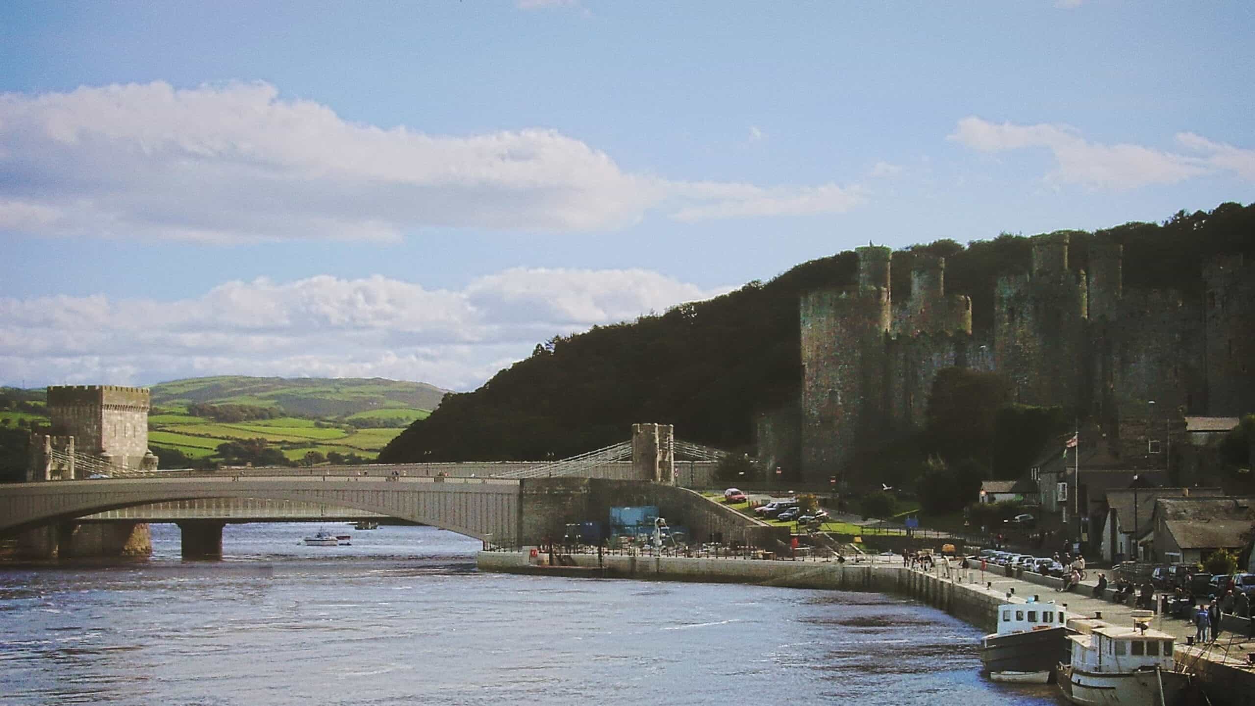 Thomas Telford's elegant 1826 Conwy Suspension Bridge crossing the estuary, with Conwy Castle's towers rising behind, both framed by the river and town walls