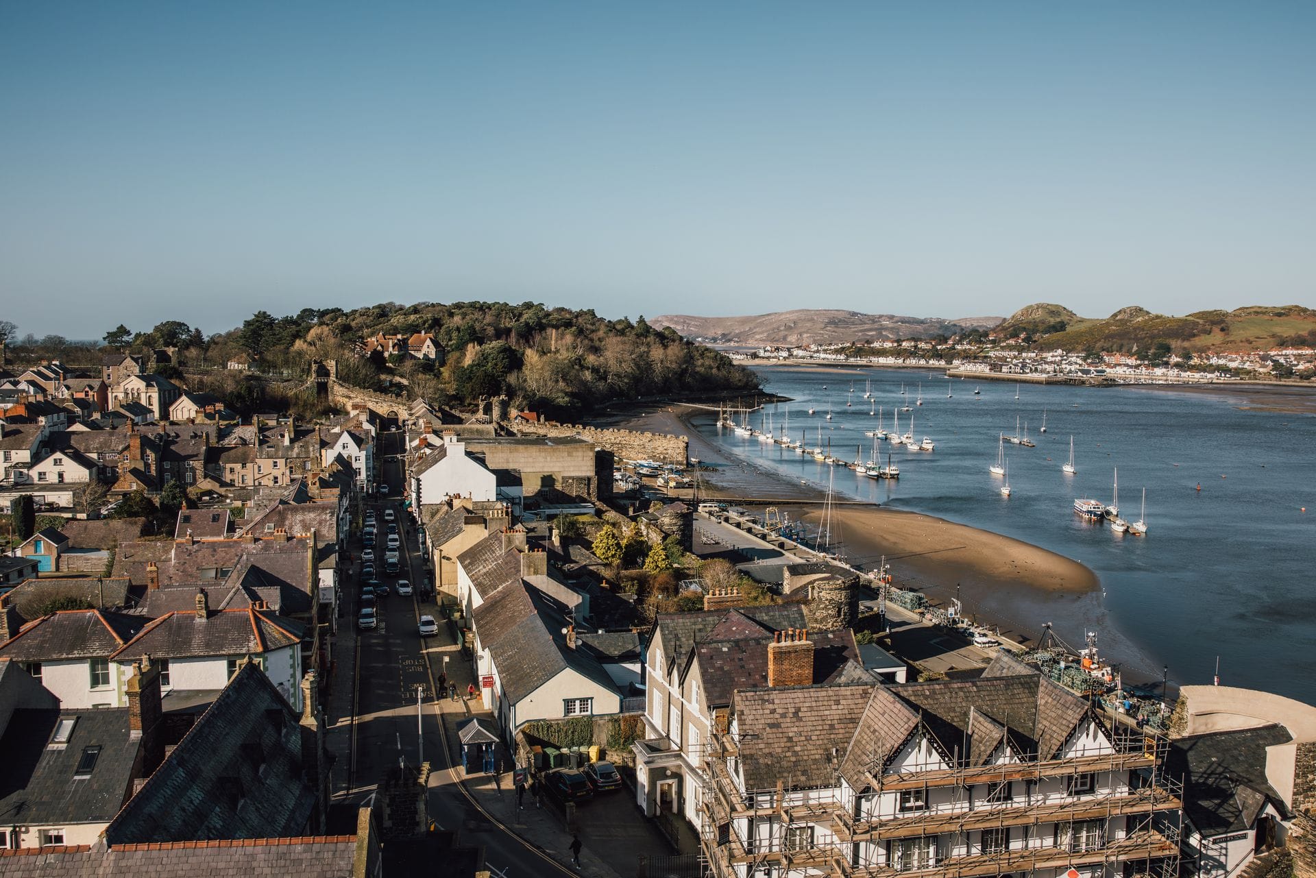 A view of Conwy from Conwy castle with the river on the right hand side and the town on the left with a bright blue sky overhead