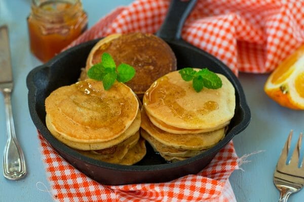 A stack of Crempog in a frying pan resting a red and white chequered table cloth