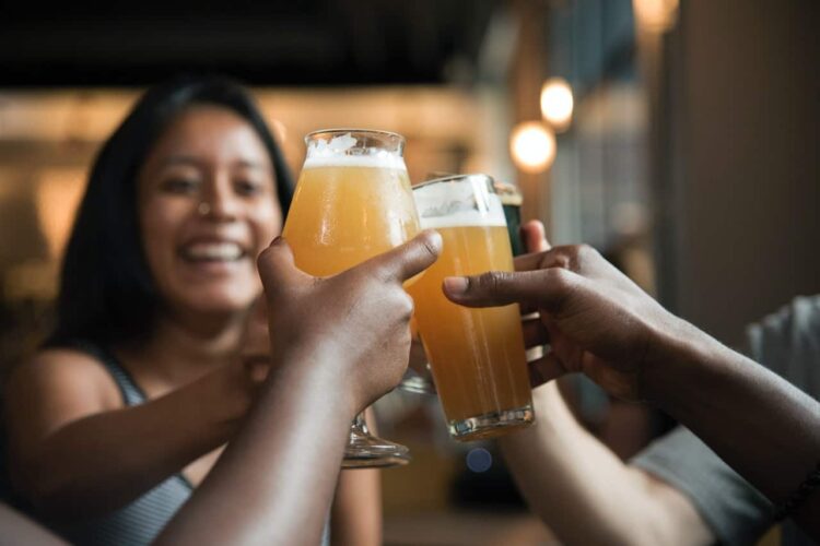 Three people clinking glasses of the best craft beer in Wales together in a toast, with a woman smiling in the background amid a warmly lit setting.
