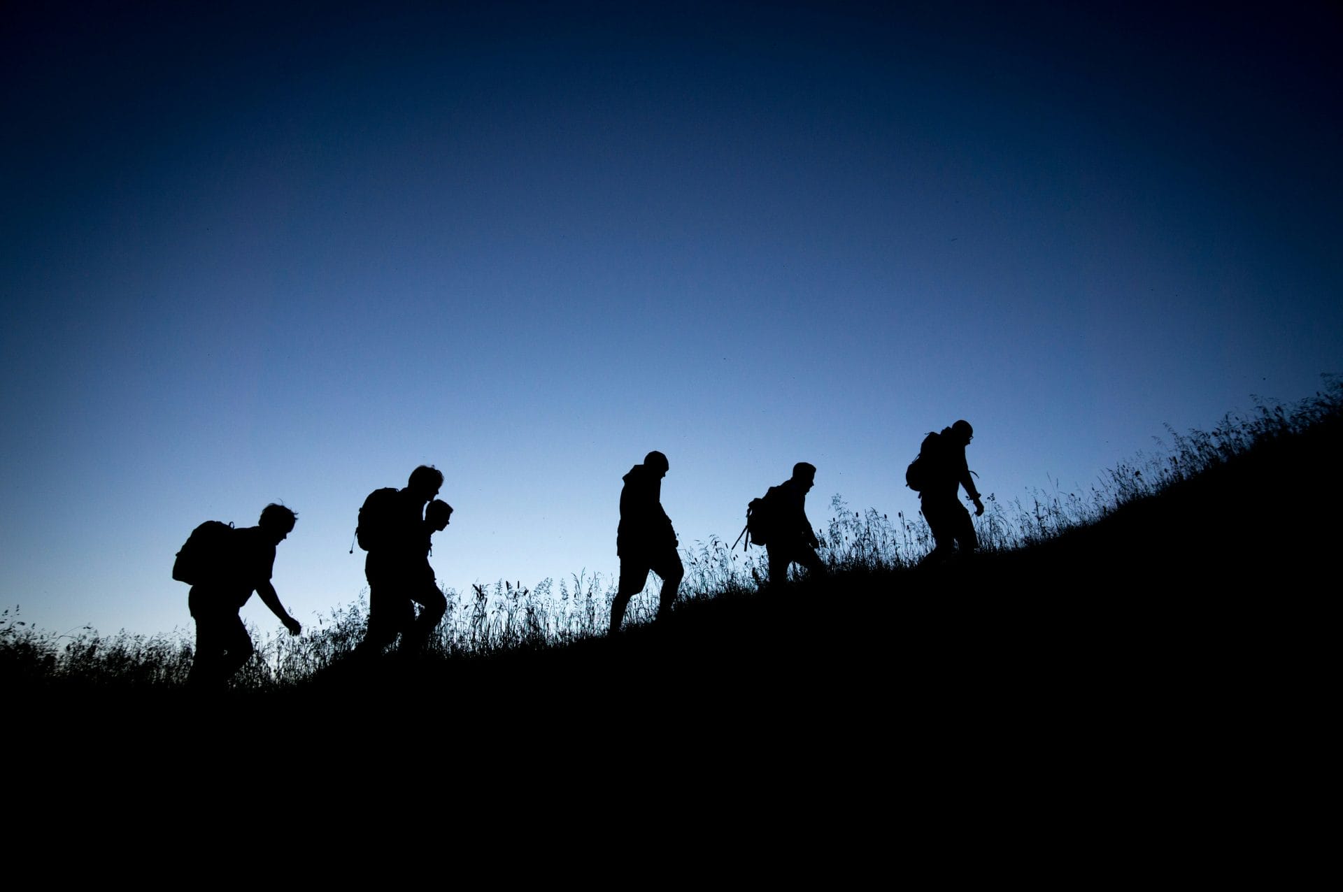 5 hikers silhouetted on a ridge at night with the light of the moon behind them
