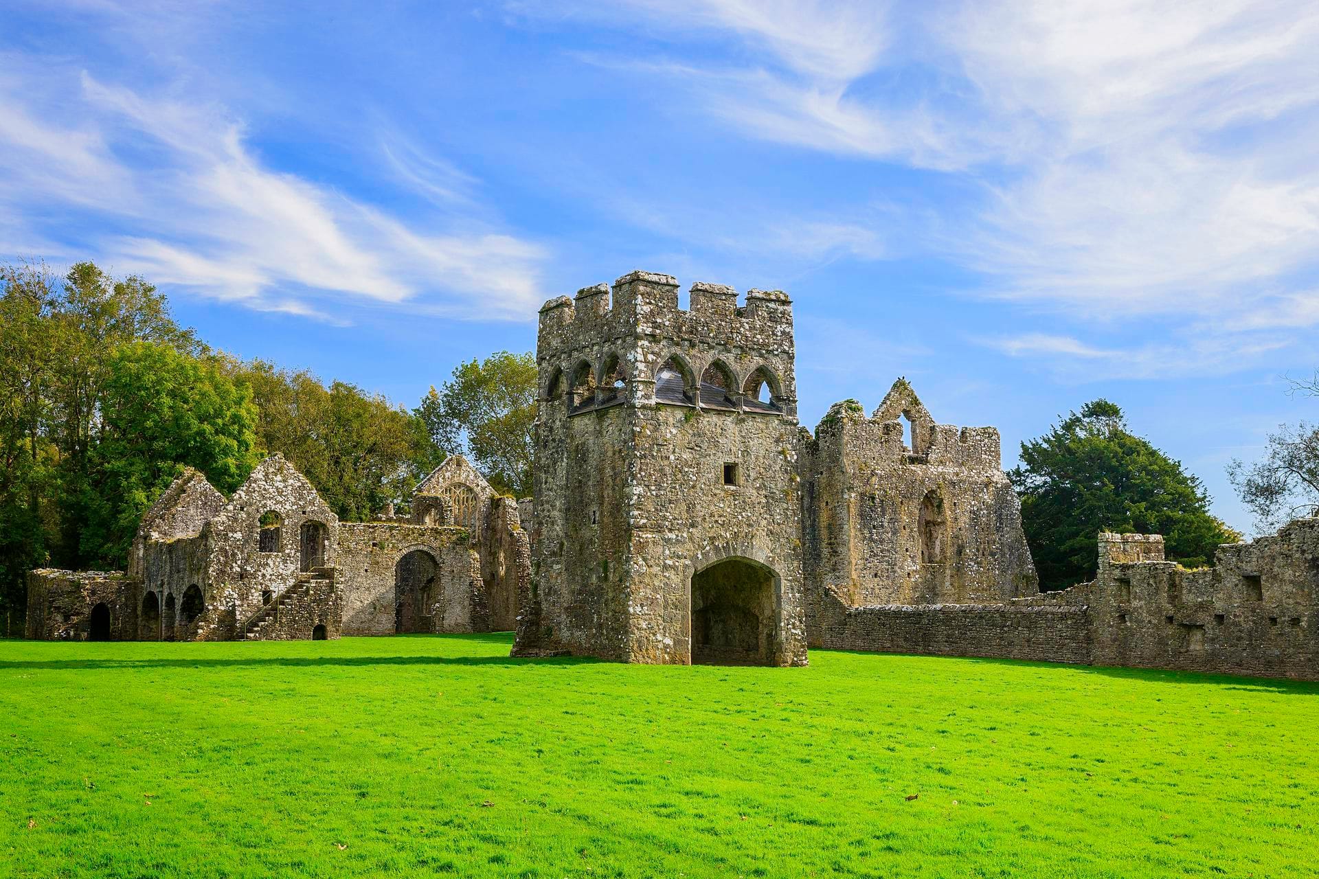 The ruined arched tower and walls of Lamphey Bishop's Palace near Pembroke, a medieval residence built for the Bishops of St Davids, set on an open lawn surrounded by trees.