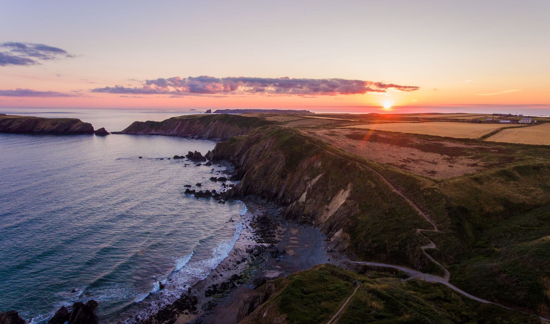 A quiet coastal path along the Pembrokeshire cliffs at golden hour and the sea calm below, evoking the secluded setting of a Pembrokeshire coast wellness retreat.