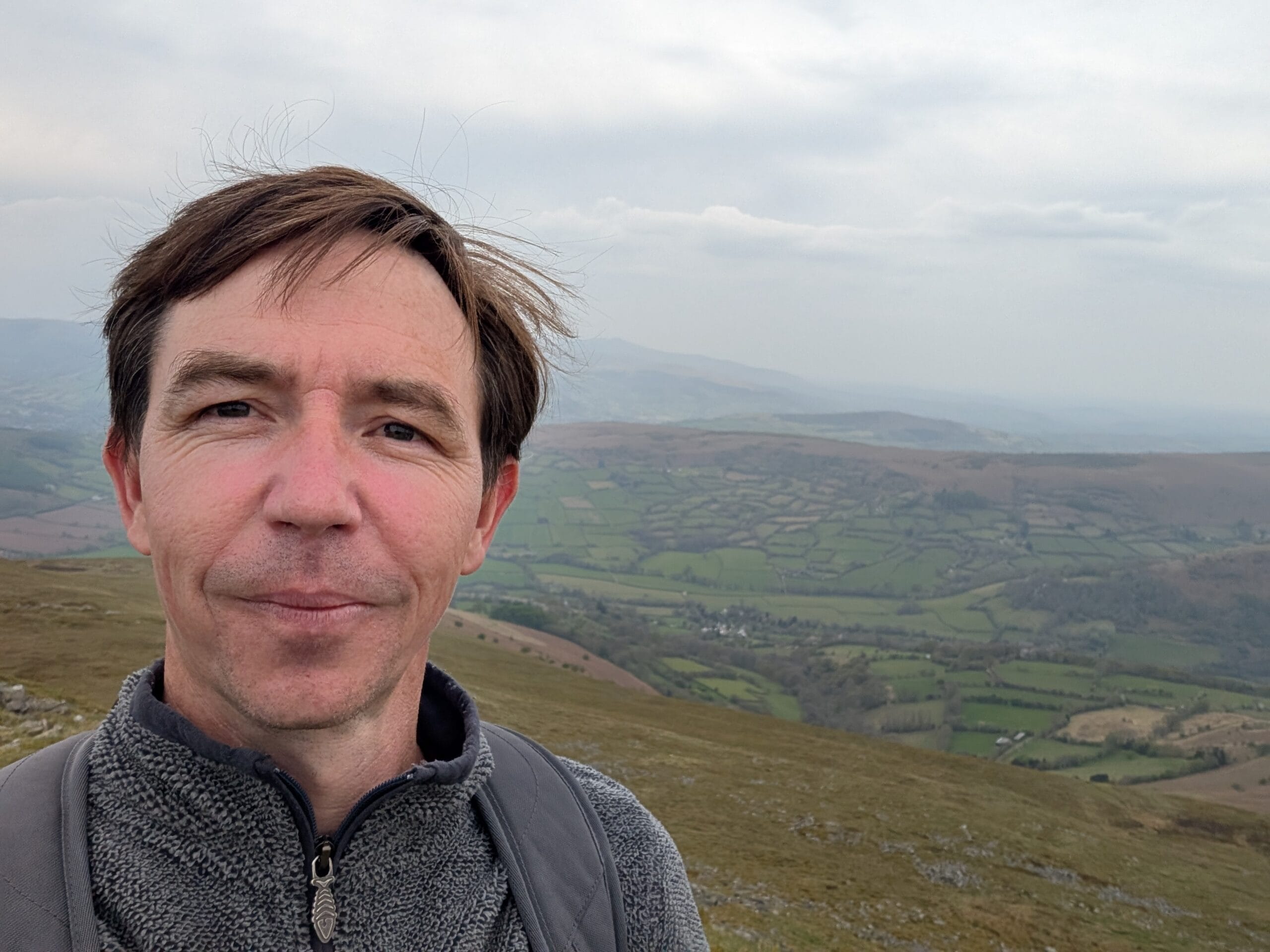 Nicholas Barrett, founder and editor of Wales.org, smiling against the dramatic backdrop of the Brecon Beacons (Bannau Brycheiniog).
