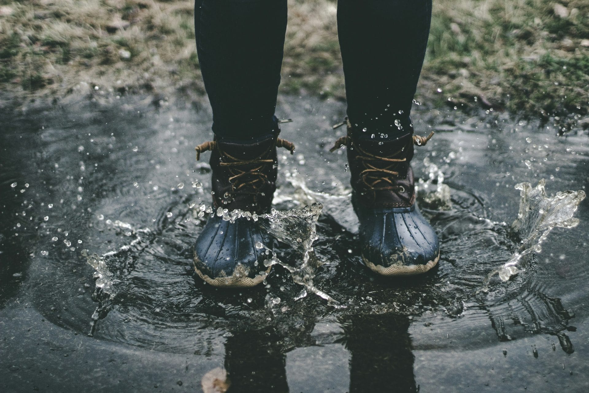 Man wearing a pair of hiking shoes, just showing the bottom legs and boots in a puddle with a splash