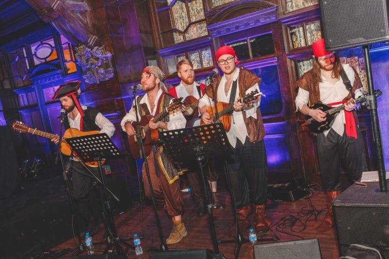 Men dressed as pirates on stage in a Welsh Theatre playing musical instruments.