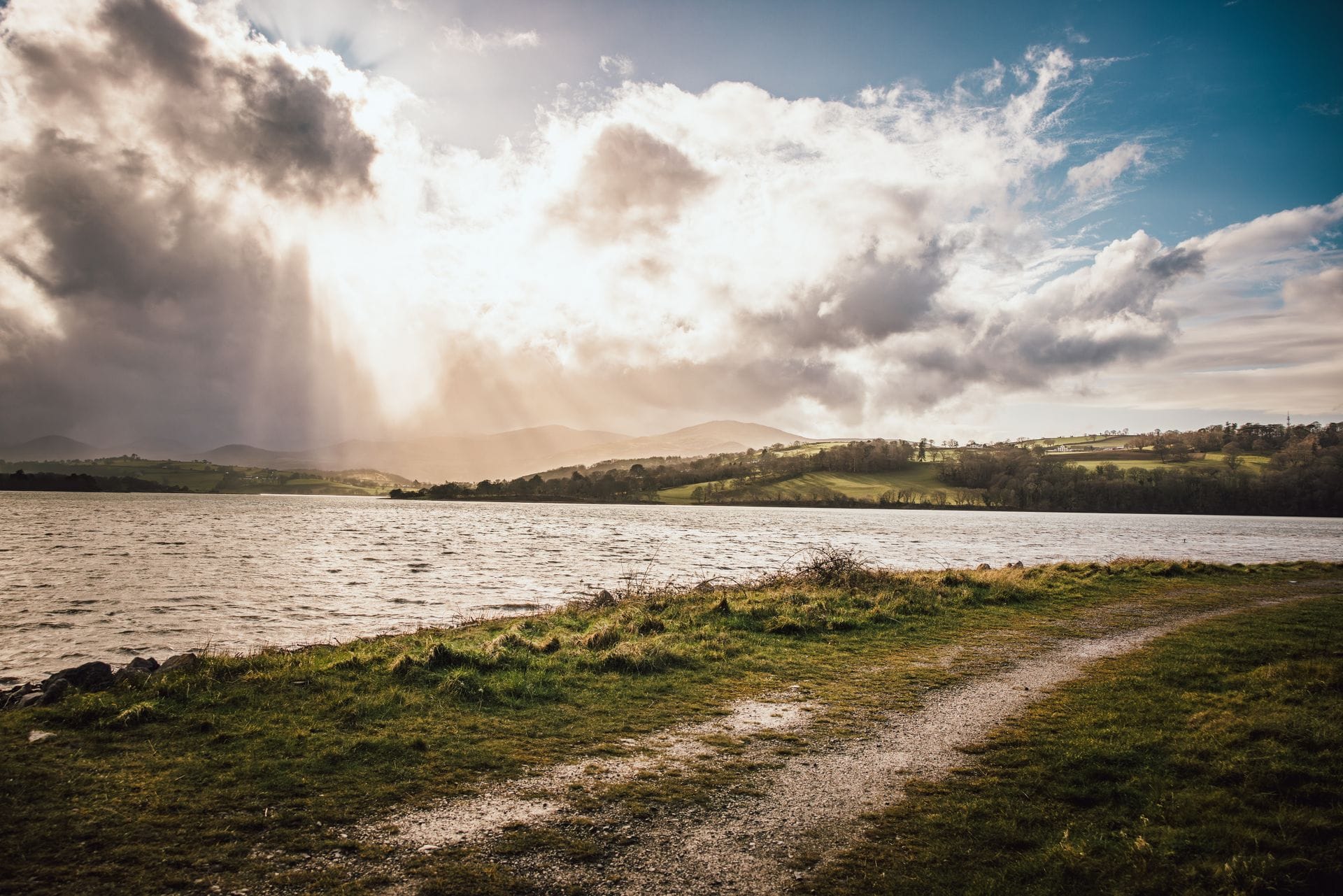 The wetland lagoons and reedbeds of RSPB Conwy nature reserve under a wide sky, with reed-fringed water reflecting the clouds and distant hills