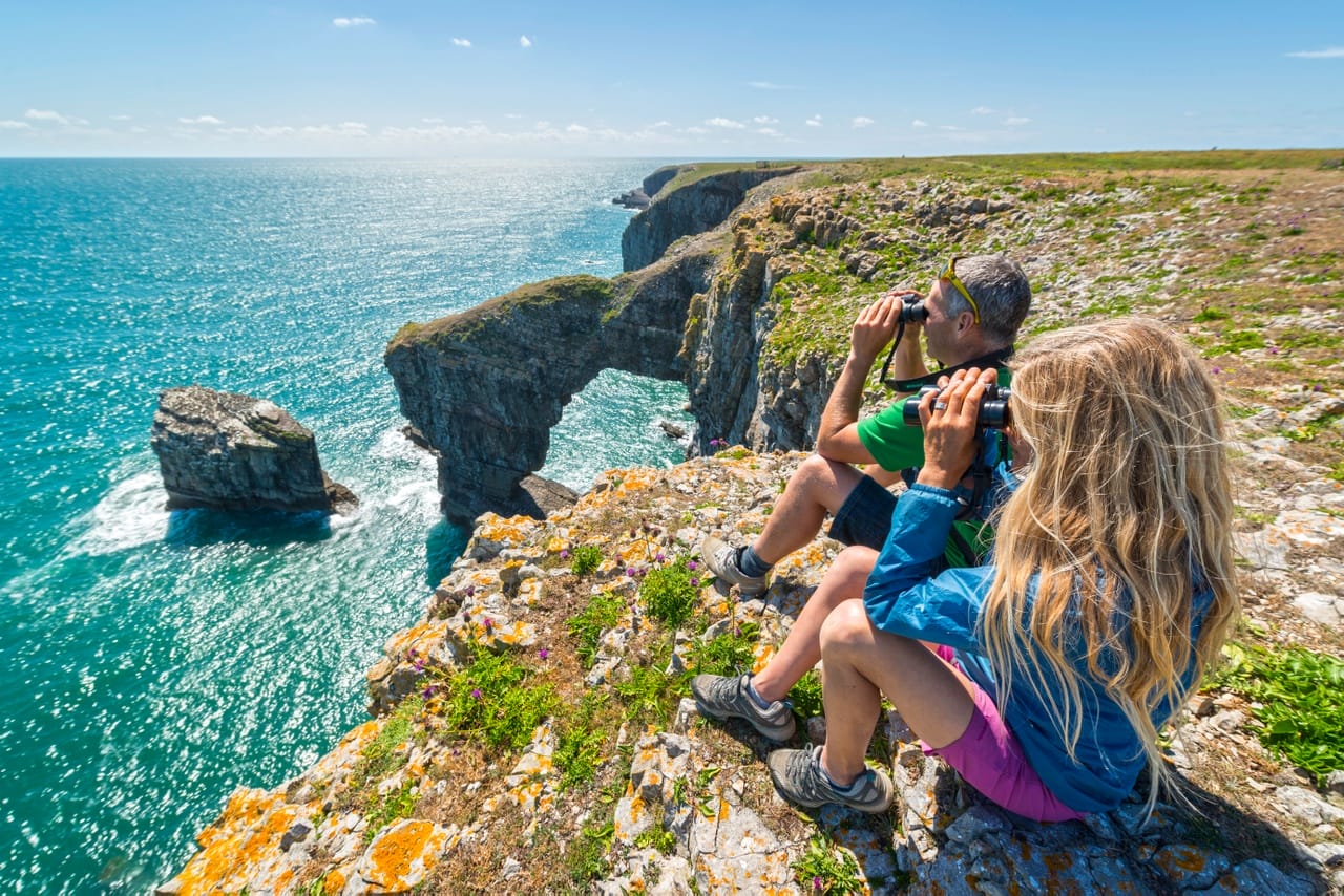 Couple birdwatching Green Bridge of Wales in Pembrokeshire