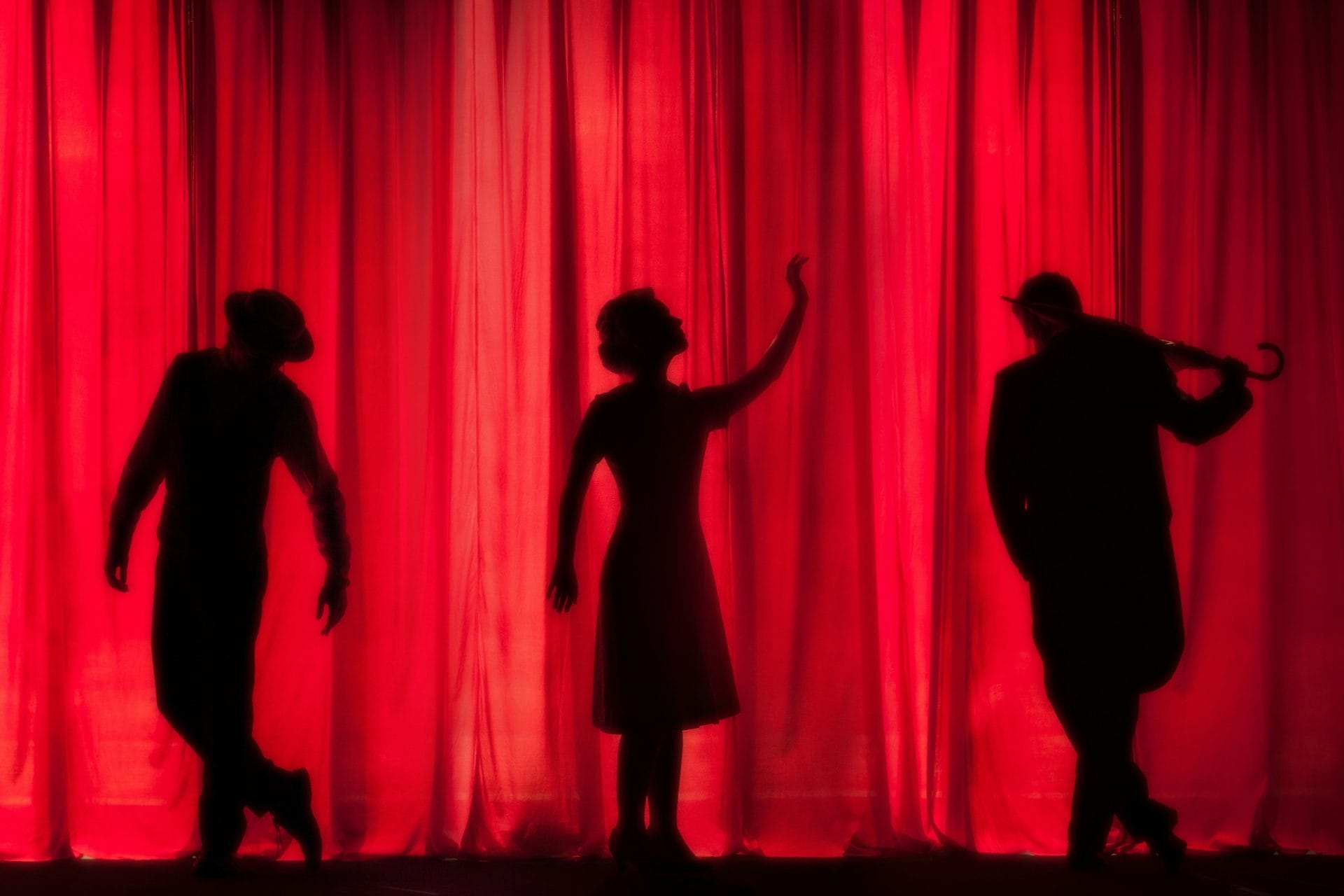 silhouette of actors behind a red curtail at the theatre