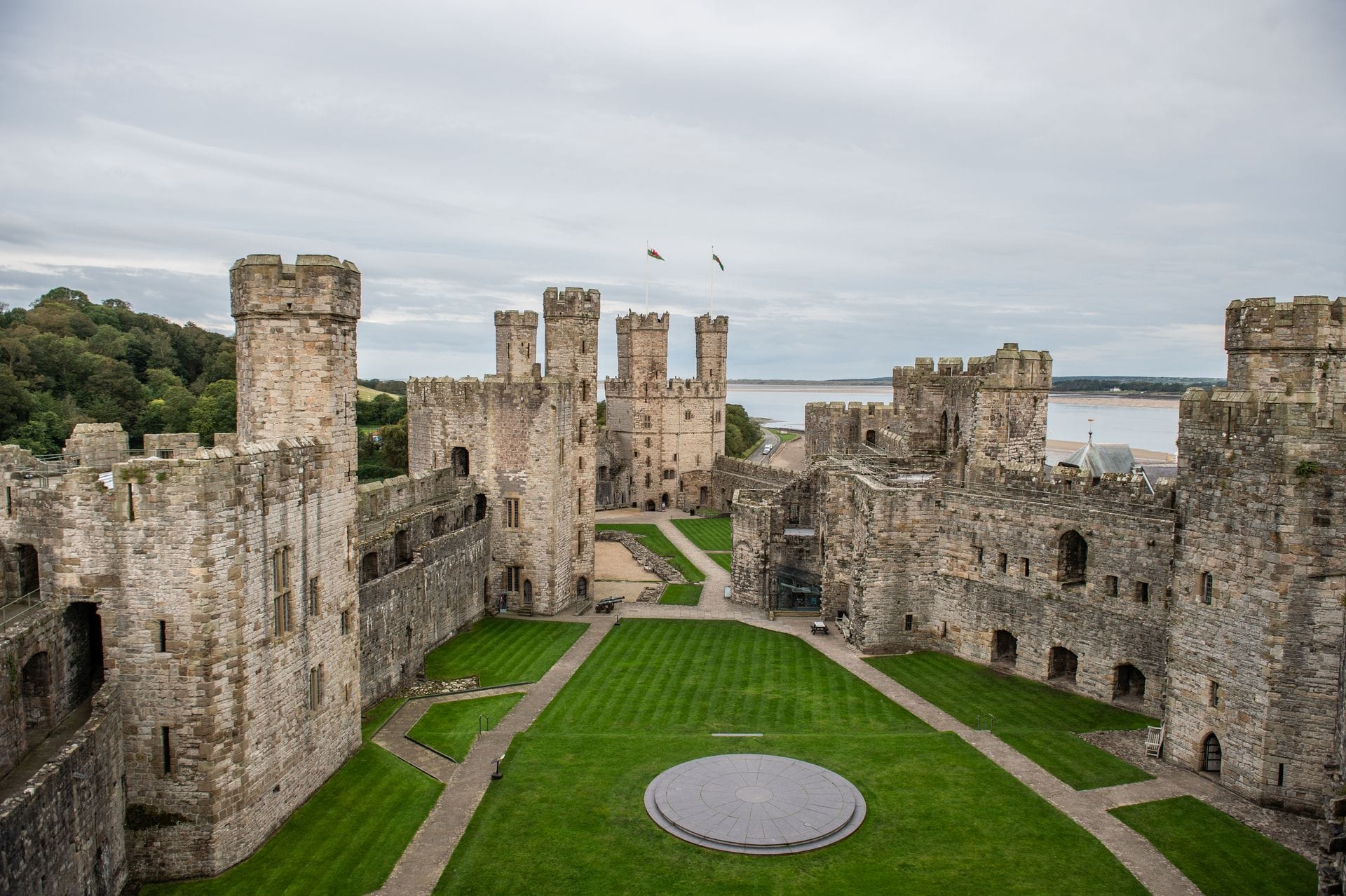 A view across Caernarfon Castle's grassy inner ward from atop one of its towers, looking toward the twin-turreted gatehouse at the far end with the Menai Strait beyond.