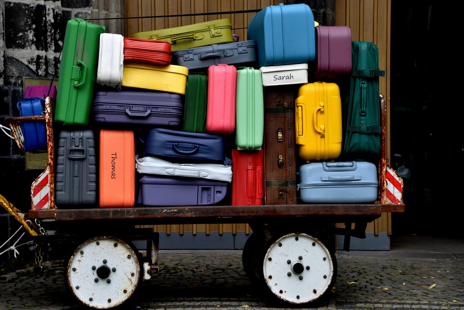 A large, colourful stack of suitcases piled high on a rustic wooden cart, illustrating the daily luggage transfer service provided on self-guided walking holidays in Wales