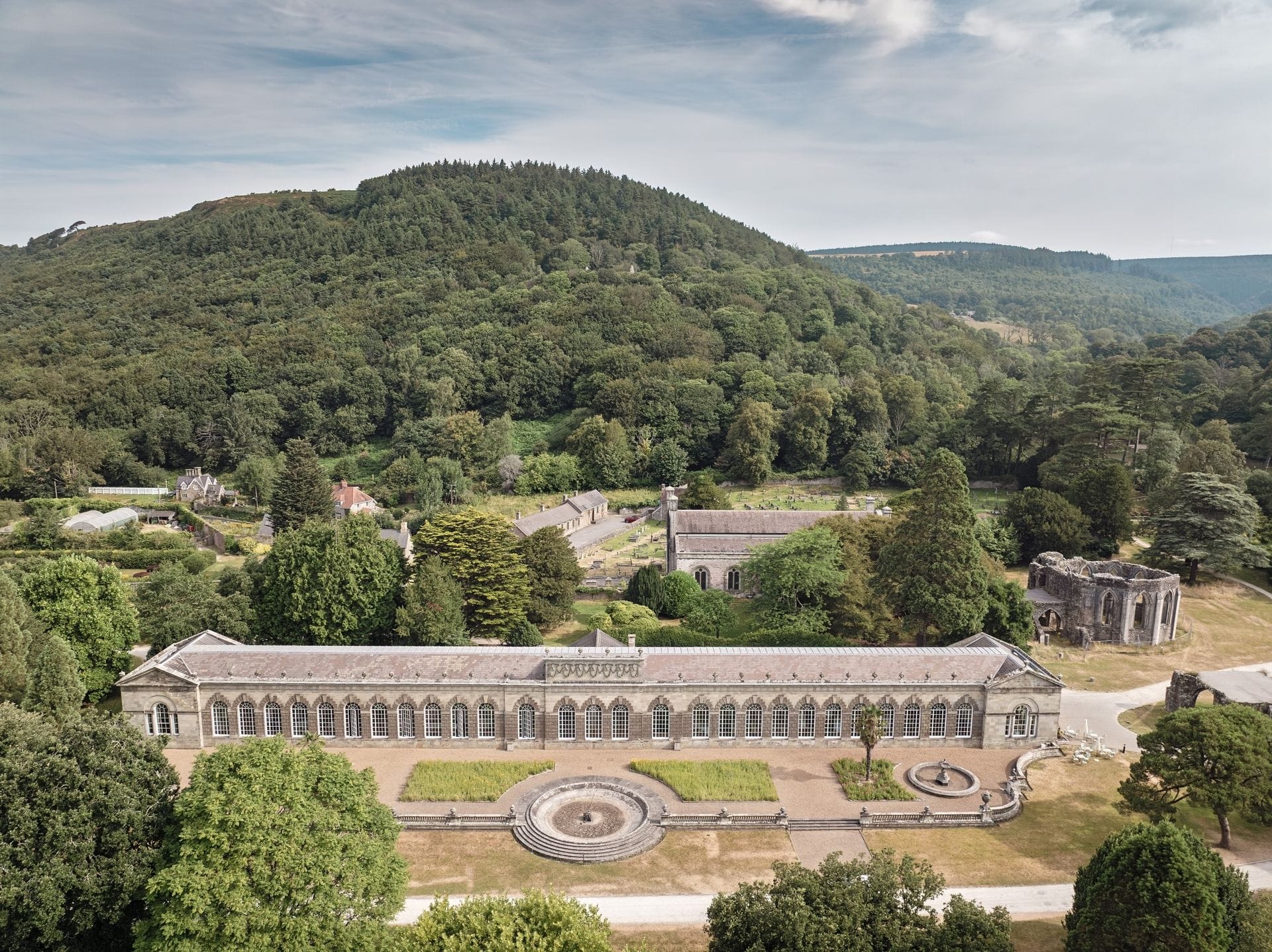 Aerial view of the Margam Orangery and the ruined chapter house of Margam Abbey, framed by wooded hills in Margam Country Park