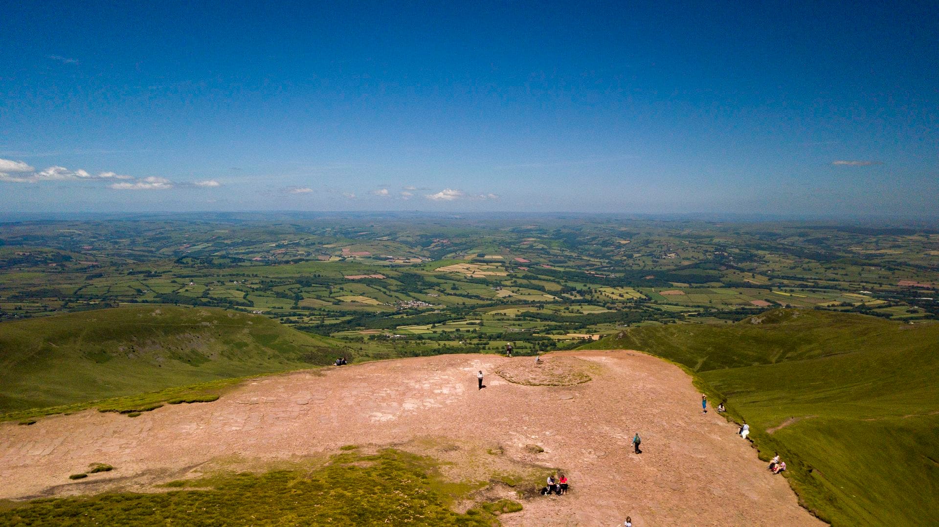 Hikers pausing on a stone path along a scenic ridge with panoramic views of the Brecon Beacons valleys.