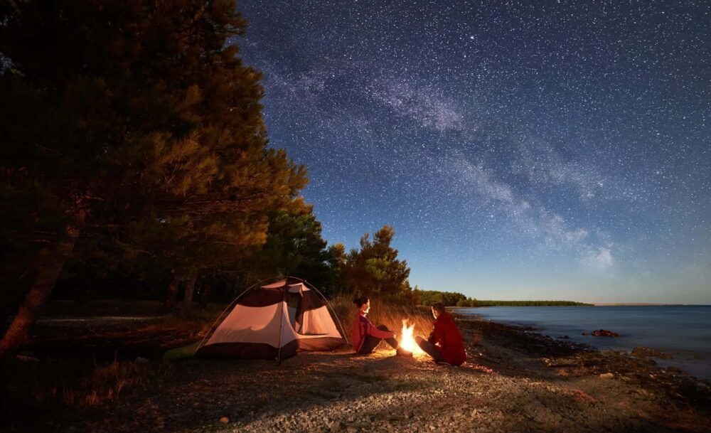 A couple around a camp fire on the beach in Wales at night with the stars shining