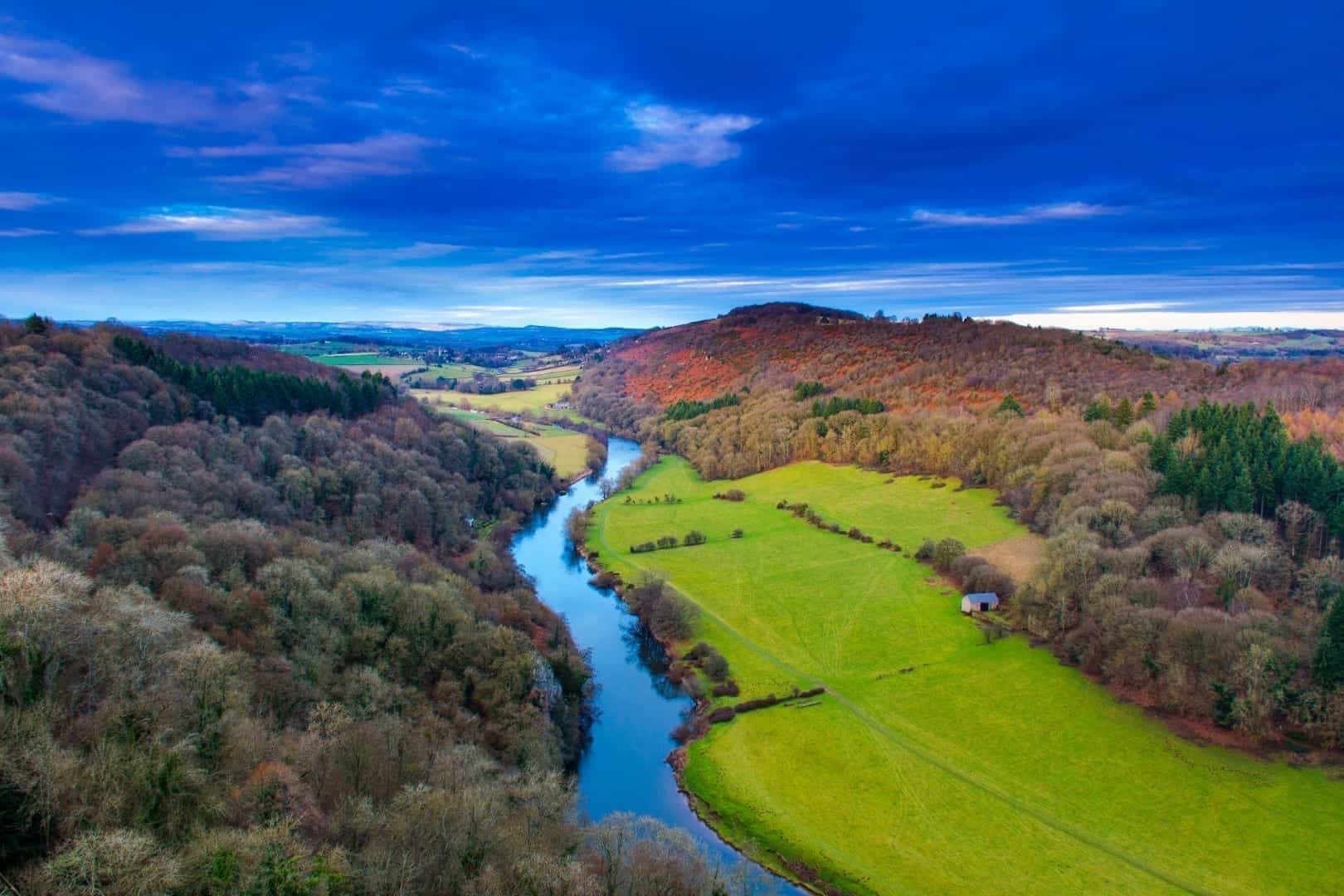 Arial view over the river Wye, with woods on either side and a dark blue and cloudy sky overhead. The perfect spot to go coarse fishing in Wales