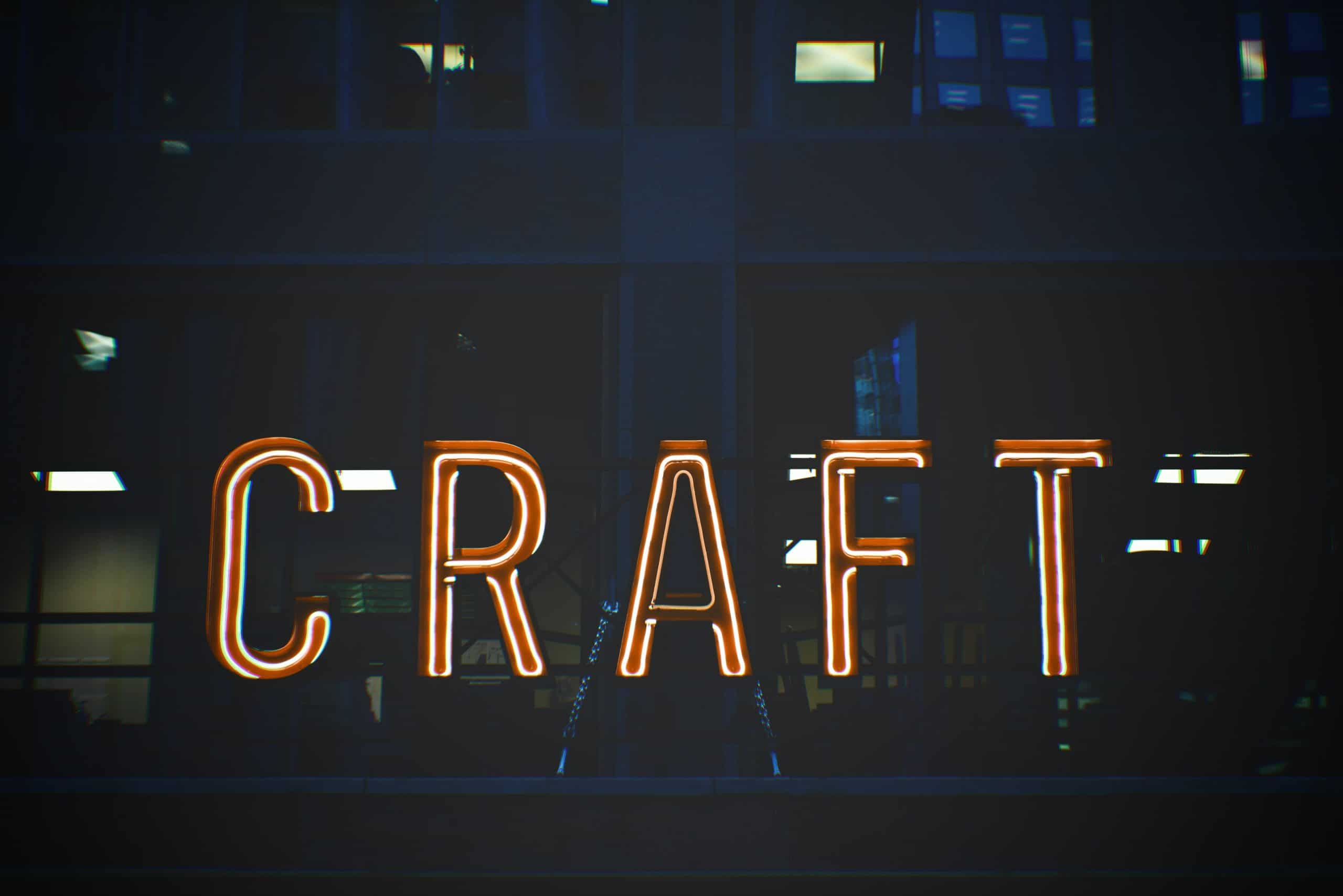 A bright orange neon sign spelling the word 'CRAFT' glowing in a dark pub window at night. Exploring local independent bars like this is the perfect way to discover the best craft beer in South Wales.