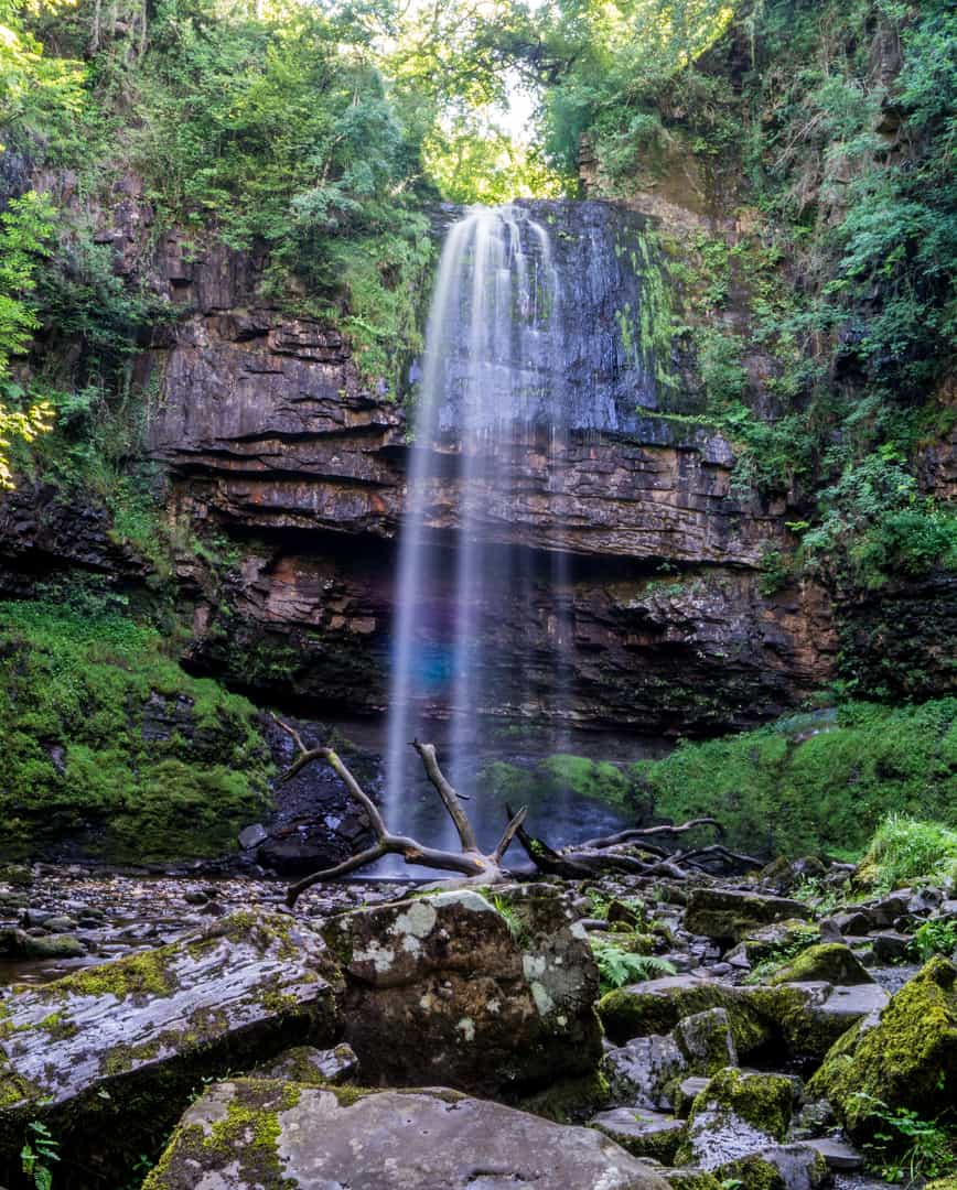 A stunning waterfall cascading over a rocky cliff face into a forest pool, typical of the dramatic ancient woodland scenery found on the Four Waterfalls Walk in the Brecon Beacons (Bannau Brycheiniog).