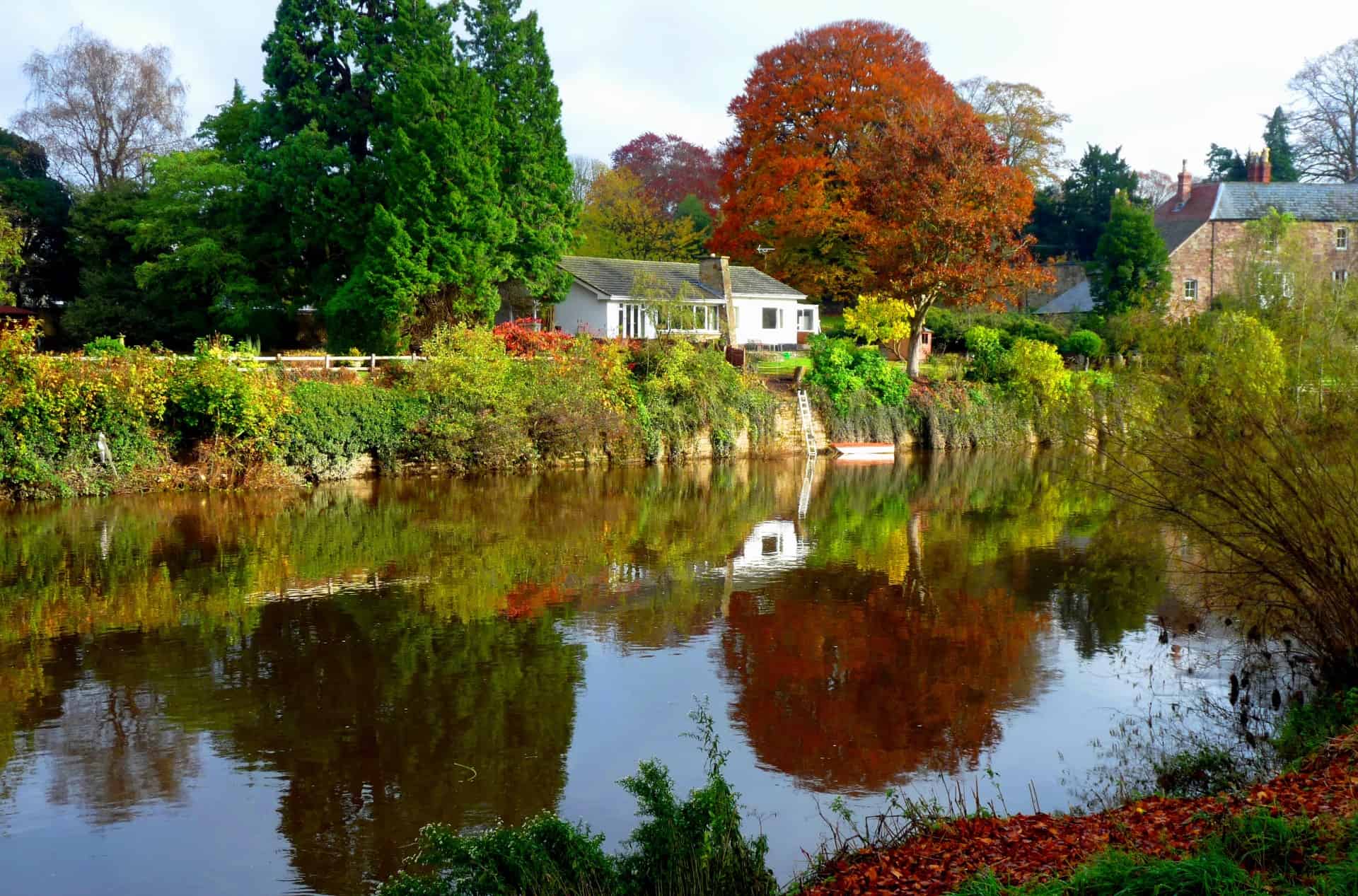 Autumn view of brown and green trees and house on the bank of a river in South Wales